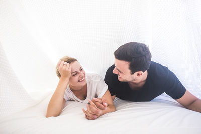Smiling woman holding hands of man while lying on bed at home