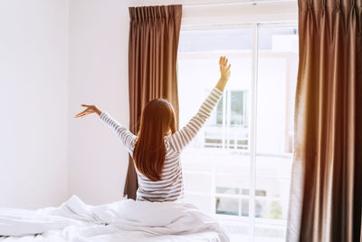 Rear view of woman sitting on bed at home