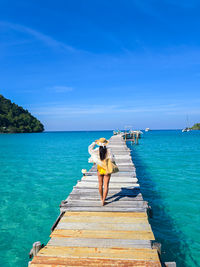 Rear view of man walking on pier over sea against blue sky