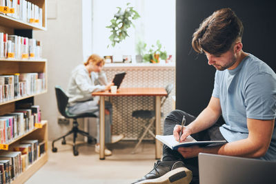 Side view of young man using mobile phone while sitting in cafe