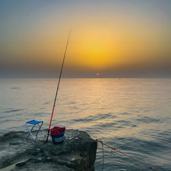 Fishing rod on rock by sea against sky during sunset