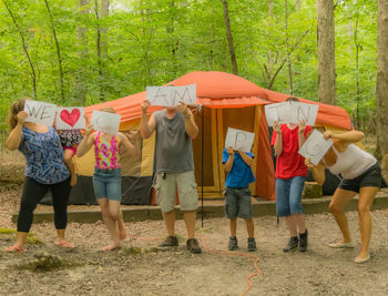 Family holding text placard while standing against tent in forest