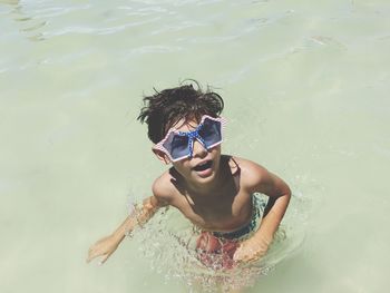 High angle view of shirtless boy wearing sunglasses in sea on sunny day