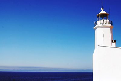 Lighthouse at seashore against blue sky 