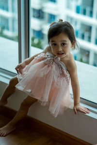 Portrait of cute girl standing against window