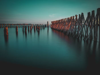 Wooden posts in sea against sky