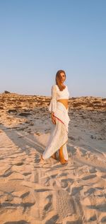 Woman wearing sunglasses on sand at beach against clear sky