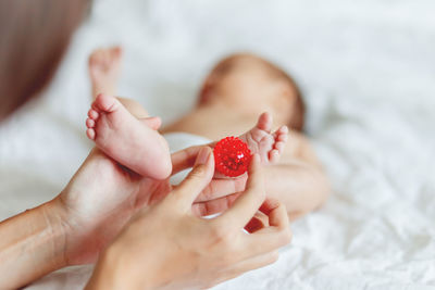 Mother holds newborn baby's feet. tiny fingers and red massage ball in woman's hand. cozy morning.