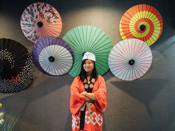 Full length portrait of woman standing against multi colored umbrella