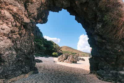 Rocky arch near beach with grass-carpeted small hills view