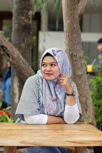 Smiling woman wearing hijab while sitting at sidewalk cafe