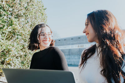 Smiling female freelancers looking at each other on sunny day