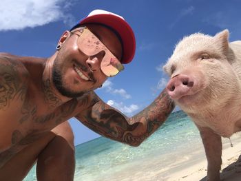 Portrait of smiling shirtless man with pig at beach