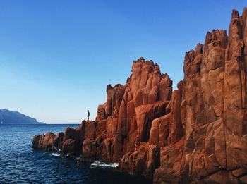 Rock formations by sea against clear blue sky