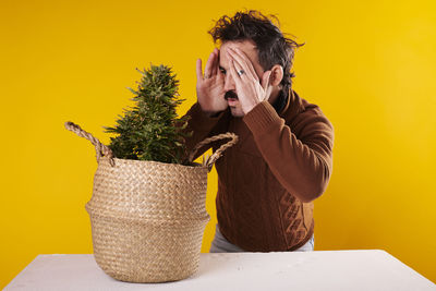 Side view of young woman sitting in wicker basket against yellow background