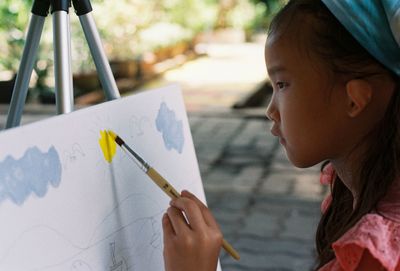 Close-up of girl painting on canvas outdoors