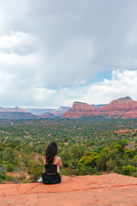 Rear view of woman sitting on mountain against sky