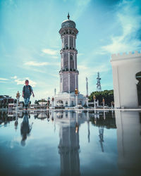 Reflection of man and building in puddle against sky