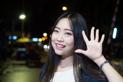 Portrait of smiling young woman showing hand in city at night