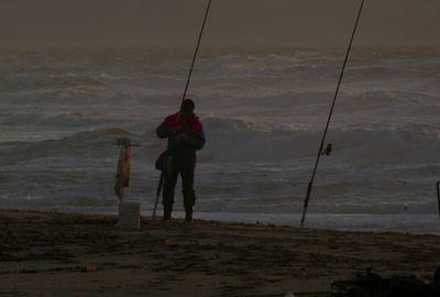 Rear view of man fishing at beach against sky