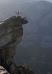 Young man raises his arms at the edge of steep cliffs in yosemite national park