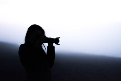 Silhouette woman photographing against sky