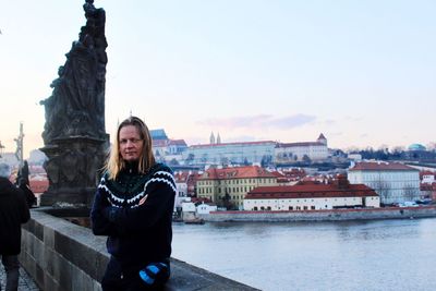 Smiling young woman standing by river in city against sky