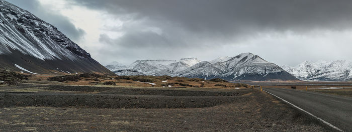 Scenic panoramic view of a deserted stretch of road winds along the base of snow covered mountains
