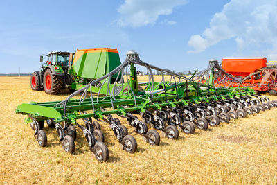 Agricultural seeders attached to tractors stand on yellow stubble in a wide field against summer day