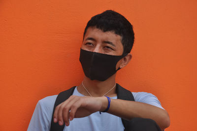 Young man wearing mask against orange background