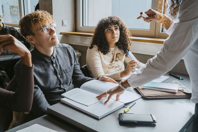 Midsection of teacher assisting young students in classroom at university