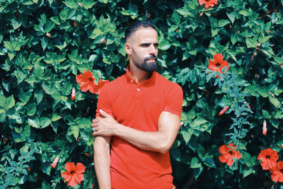 Young man looking away while standing against plants during sunny day