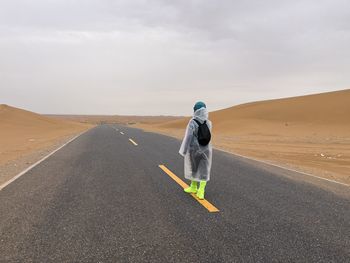 Rear view of man walking on road against sky