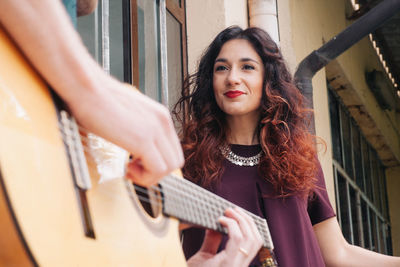 Low angle view of smiling woman by man playing guitar