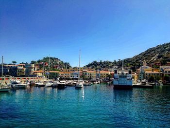 Sailboats moored in harbor by buildings against clear blue sky