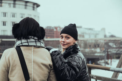 Portrait of confident smiling woman wearing warm clothing while standing with friend in city during winter