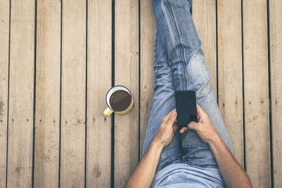 Low section of man using mobile phone while sitting on wood