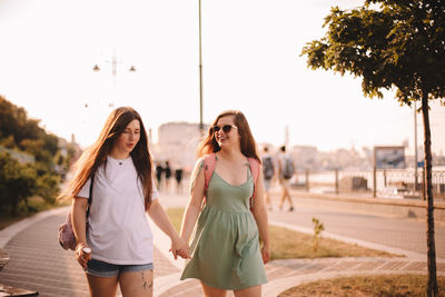 Lesbian couple talking while walking in city holding hands in summer