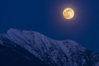 The full moon rises above snow covered mountain peaks on a spring night in the coast mountains of british columbia.