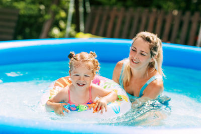 A young mother teaches her little daughter to swim in the pool in the garden 