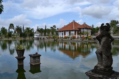 Statue by lake and buildings against sky