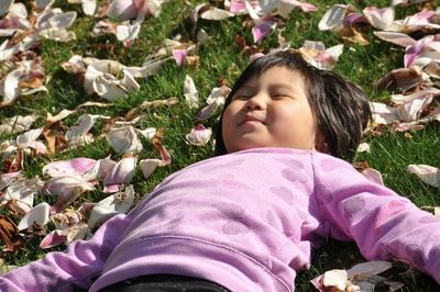 Low angle view of girl lying on grass with pink petals