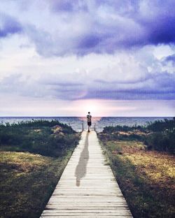 Rear view of man walking on road against cloudy sky