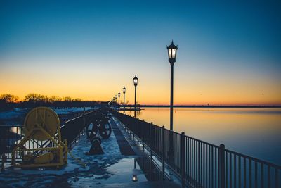 Street light by sea against clear sky during sunset