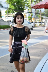 Portrait of woman on street with plastic bag in city