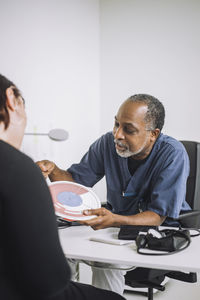 Mature male doctor discussing over in vitro fertilization chart with female patient sitting at desk in medical clinic