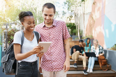 Portrait of smiling friends using digital tablet while sitting on table