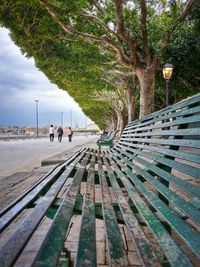 Benches by people walking on footpath against sky