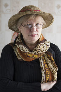 Portrait of senior woman wearing hat sitting against wall at home