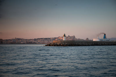 Buildings by sea against clear sky during sunset